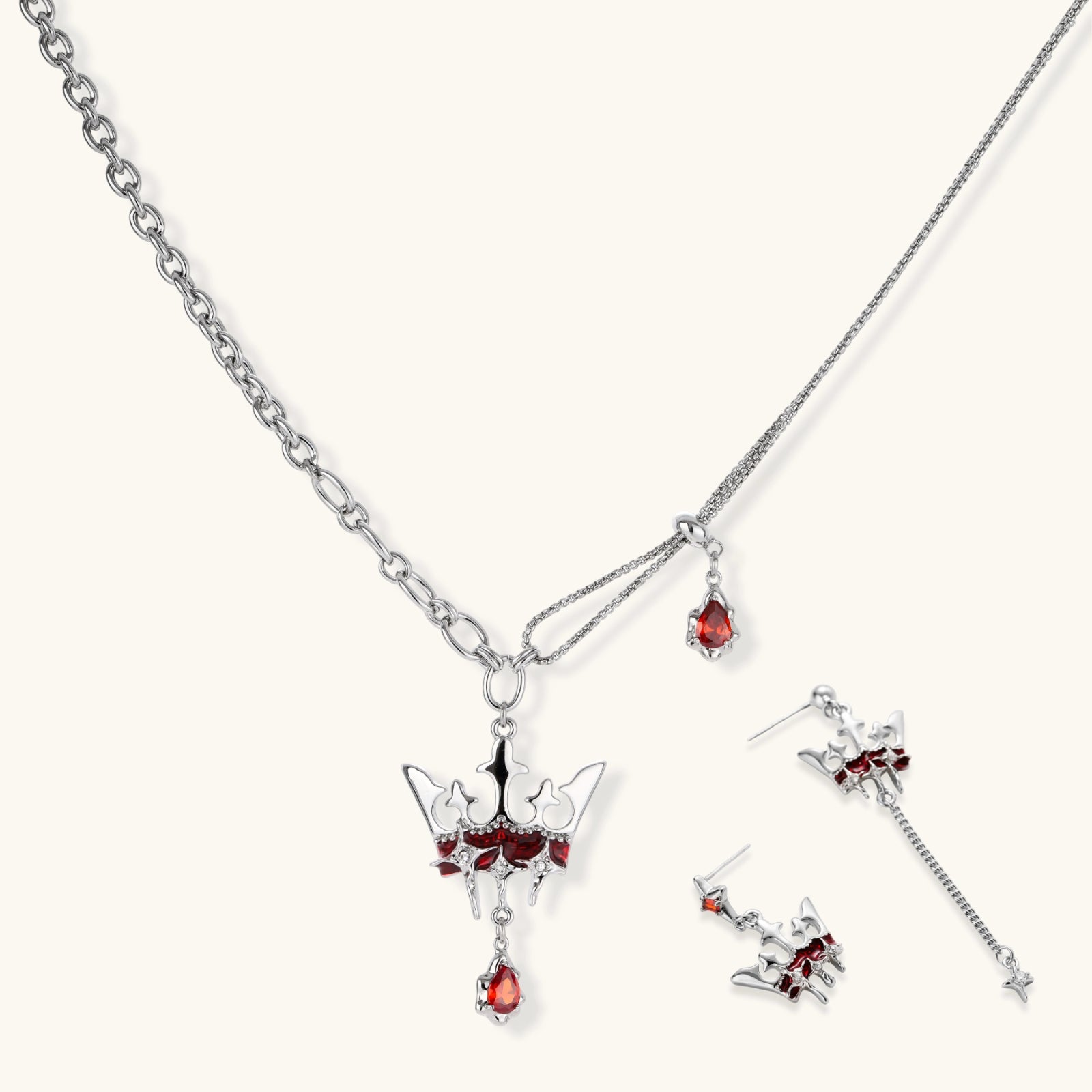 Silver-tone crown pendant with red zirconia stones and matching asymmetrical earrings on cream background