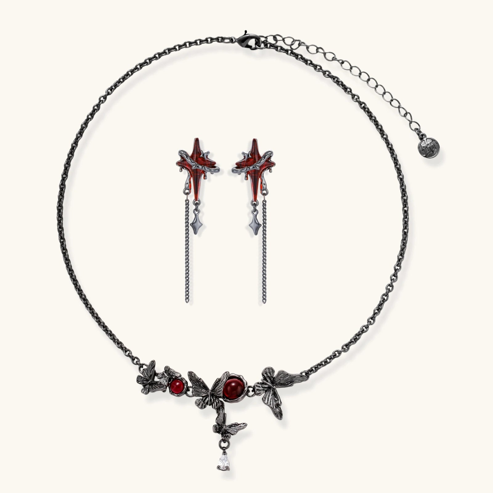 Gothic jewelry set with red resin cross pendants wrapped in dark metal chains on cream background.