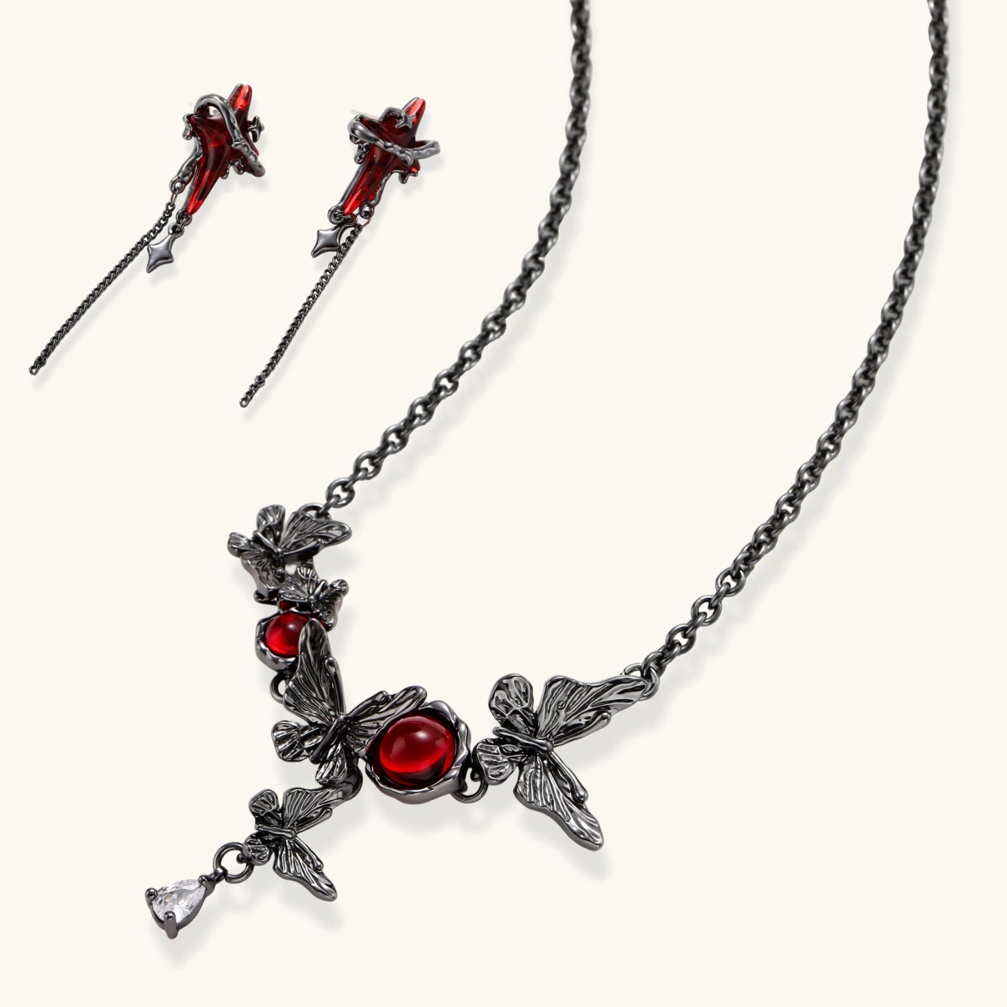 Gothic jewelry set with red resin cross pendants wrapped in dark metal chains on cream background.
